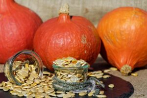 Semillas de calabaza en tarros de cristal frente a tres calabazas naranjas sobre arpillera