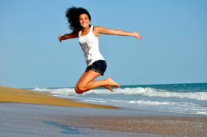 Mujer sonriente saltando con los brazos abiertos en la playa junto al mar