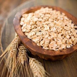 Copos de avena en un cuenco de madera con espigas de trigo sobre mesa rústica