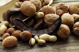Frutos secos variados con nueces, almendras, avellanas, cacahuetes, pistachos y algarroba sobre madera