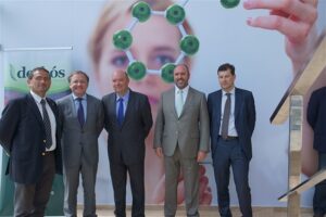 Cinco hombres con traje posando ante un panel del laboratorio Derbós durante una visita institucional