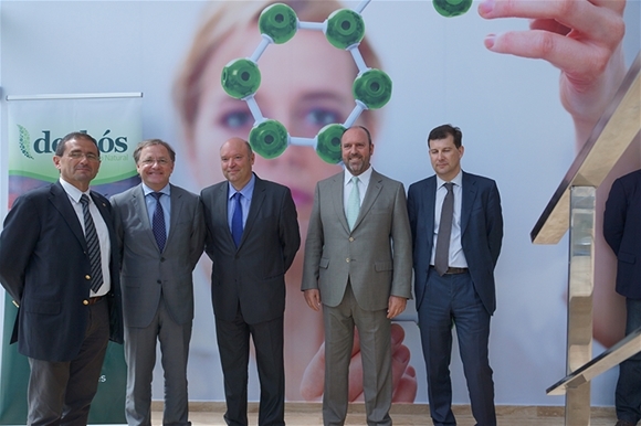 Cinco hombres con traje posando ante un panel del laboratorio Derbós durante una visita institucional
