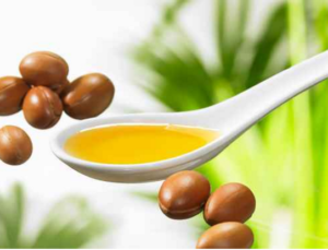Cuchara blanca con aceite de argán dorado junto a semillas de argán y fondo verde natural