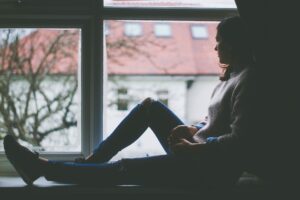 Mujer pensativa sentada junto a la ventana mirando al exterior con gesto melancólico