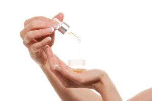 Manos con manicura sostienen frasco con gotero de aceite cosmético natural