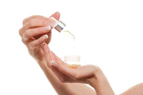 Manos con manicura sostienen frasco con gotero de aceite cosmético natural
