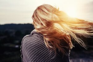 Mujer de espaldas con cabello rubio al viento iluminado por la luz del atardecer