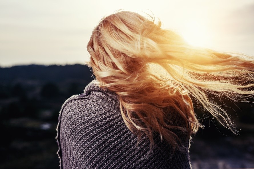 Mujer de espaldas con cabello rubio al viento iluminado por la luz del atardecer