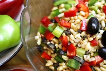 Ensalada fresca de trigo con pimiento rojo y verde, apio y aceitunas negras en bol de cristal