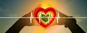 Manos formando un corazón sobre un corazón rojo con línea de electrocardiograma al atardecer