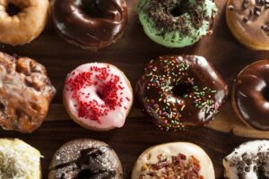 Variedad de donuts glaseados con chocolate, fresa y virutas de colores sobre mesa de madera