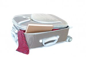 Maleta de viaje gris con ruedas medio abierta con ropa a rayas y un cuaderno asomando