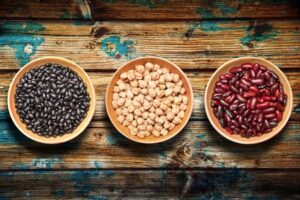 Tres cuencos con legumbres: frijoles negros, garbanzos y alubias rojas sobre madera rústica