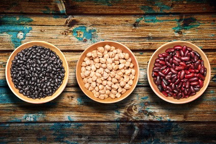 Tres cuencos con legumbres: frijoles negros, garbanzos y alubias rojas sobre madera rústica
