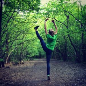 Bailarina realizando una extensión vertical de pierna en un sendero rodeado de bosque verde
