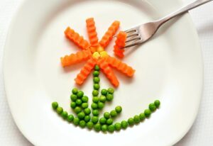 Flor hecha con zanahorias y guisantes en un plato blanco junto a un tenedor