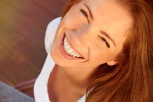 Mujer pelirroja sonriendo ampliamente con dientes blancos bajo luz cálida