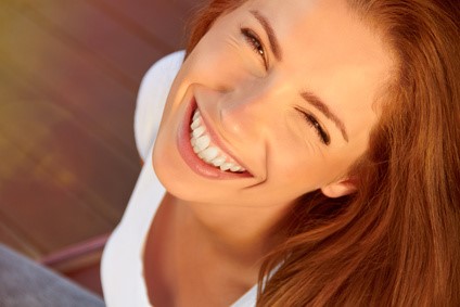 Mujer pelirroja sonriendo ampliamente con dientes blancos bajo luz cálida