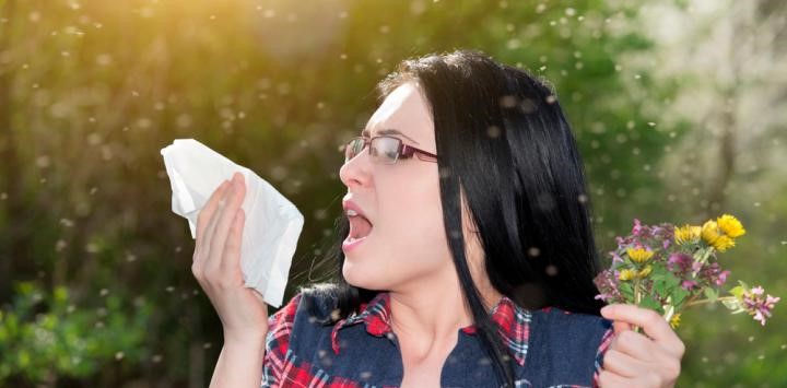 Mujer con pañuelo estornudando por alergia al polen mientras sostiene un ramo de flores