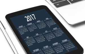 Tablet mostrando un calendario anual de 2017 junto a un portátil sobre mesa blanca