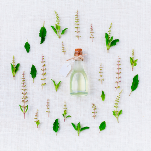 Botella de aceite esencial con etiqueta rodeada de hojas y flores de albahaca sobre lino blanco