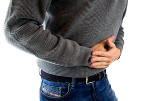 Hombre con jersey gris sujetándose el abdomen con las manos por dolor o molestias de gases