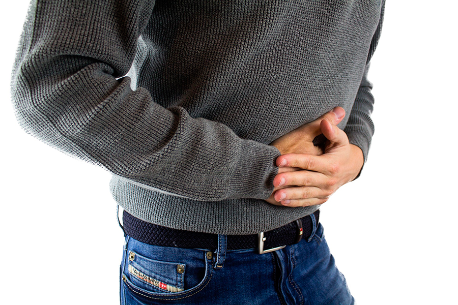 Hombre con jersey gris sujetándose el abdomen con las manos por dolor o molestias de gases