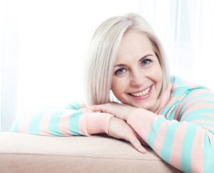 Mujer rubia sonriente apoyada en un sofá con jersey de rayas pastel