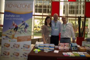 Tres personas sonrientes en un stand con productos Royaltone y complementos alimenticios sobre la mesa