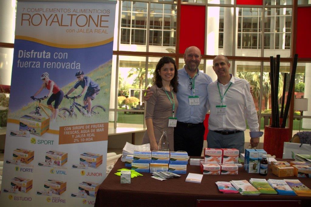 Tres personas sonrientes en un stand con productos Royaltone y complementos alimenticios sobre la mesa