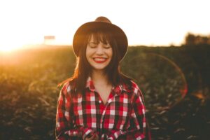 Mujer sonriente con camisa de cuadros y sombrero en un campo al atardecer