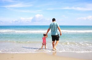 Padre e hija caminando de la mano por la orilla del mar en un día soleado