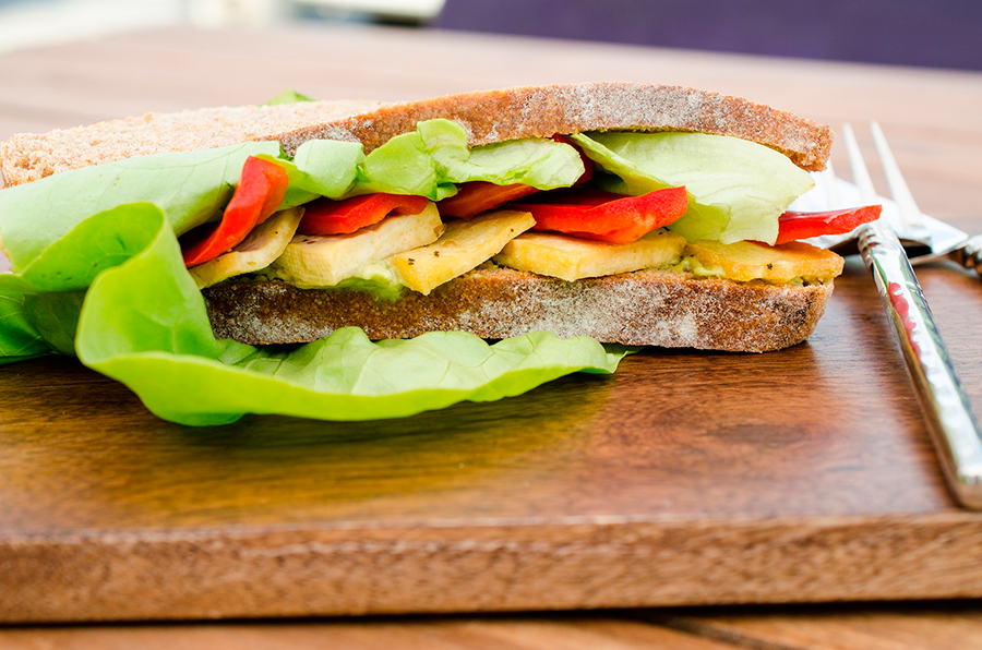 Sándwich de pan integral con tofu, lechuga y pimiento rojo sobre tabla de madera