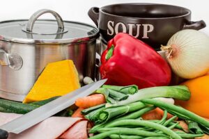 Olla y bol de sopa junto a verduras frescas: pimiento, cebolla, calabaza, zanahorias y cuchillo
