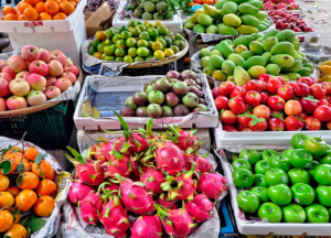 Puesto de mercado con frutas variadas: manzanas, mangos, mandarinas, pitahayas y caimitos en cajas