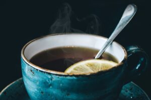 Taza azul de té caliente humeante con una rodaja de limón y cuchara sobre fondo oscuro