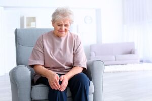 Mujer mayor sentada en un sillón sujetándose la rodilla con gesto de dolor