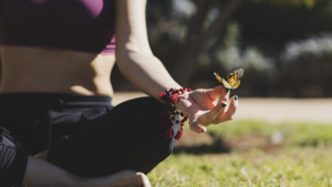 Mujer en postura de meditación en el parque con una mariposa monarca posada en su dedo