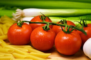 Tomates rojos en rama con gotas de agua junto a macarrones y cebolletas frescas