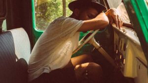 Hombre con sombrero apoyado sobre el volante de una vieja furgoneta verde, cansado