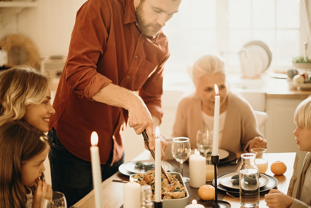 Hombre trinchando el asado en una cena familiar con velas mientras la familia observa alrededor de la mesa