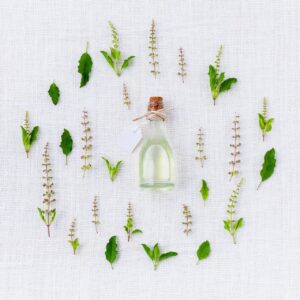 Botella de aceite esencial con etiqueta rodeada de hojas y flores de albahaca sobre tela blanca