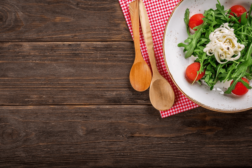 Ensalada de rúcula, tomates cherry y queso en plato blanco sobre mantel de cuadros y mesa de madera