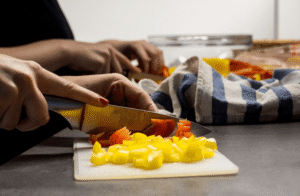 Manos cortando pimientos amarillos y rojos con un cuchillo sobre una tabla en la cocina