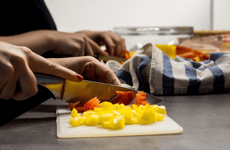 Manos cortando pimientos amarillos y rojos con un cuchillo sobre una tabla en la cocina