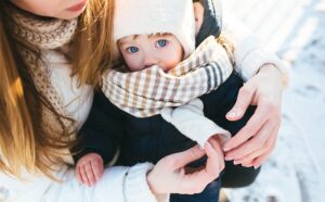 Madre abriga a su bebé de ojos azules con gorro y bufanda en un día nevado de invierno