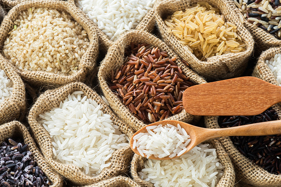 Variedades de arroz blanco, integral, rojo y negro en sacos de yute con cucharas de madera