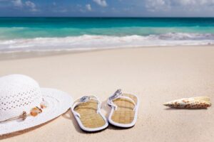 Sombrero de paja, chanclas y caracola sobre la arena de una playa con mar turquesa al fondo