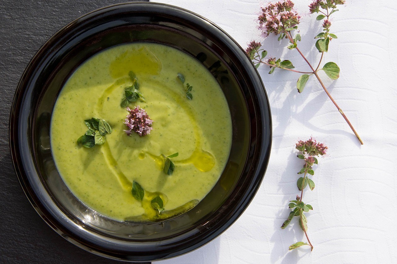 Crema de calabacín en cuenco negro decorada con orégano fresco y flores junto a ramas de orégano