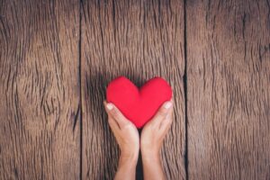 Manos sosteniendo un corazón rojo de tela sobre fondo de madera rústica